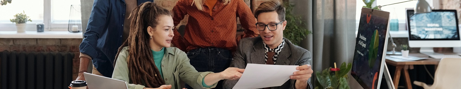 People sitting around the desk looking at paperwork and computers